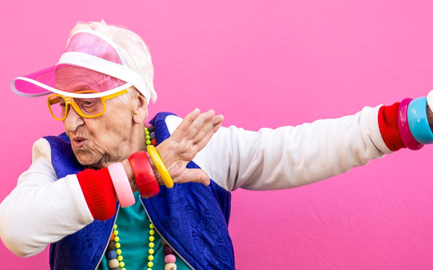 An elderly woman wearing brightly colored, hip clothing doing a funny pose.